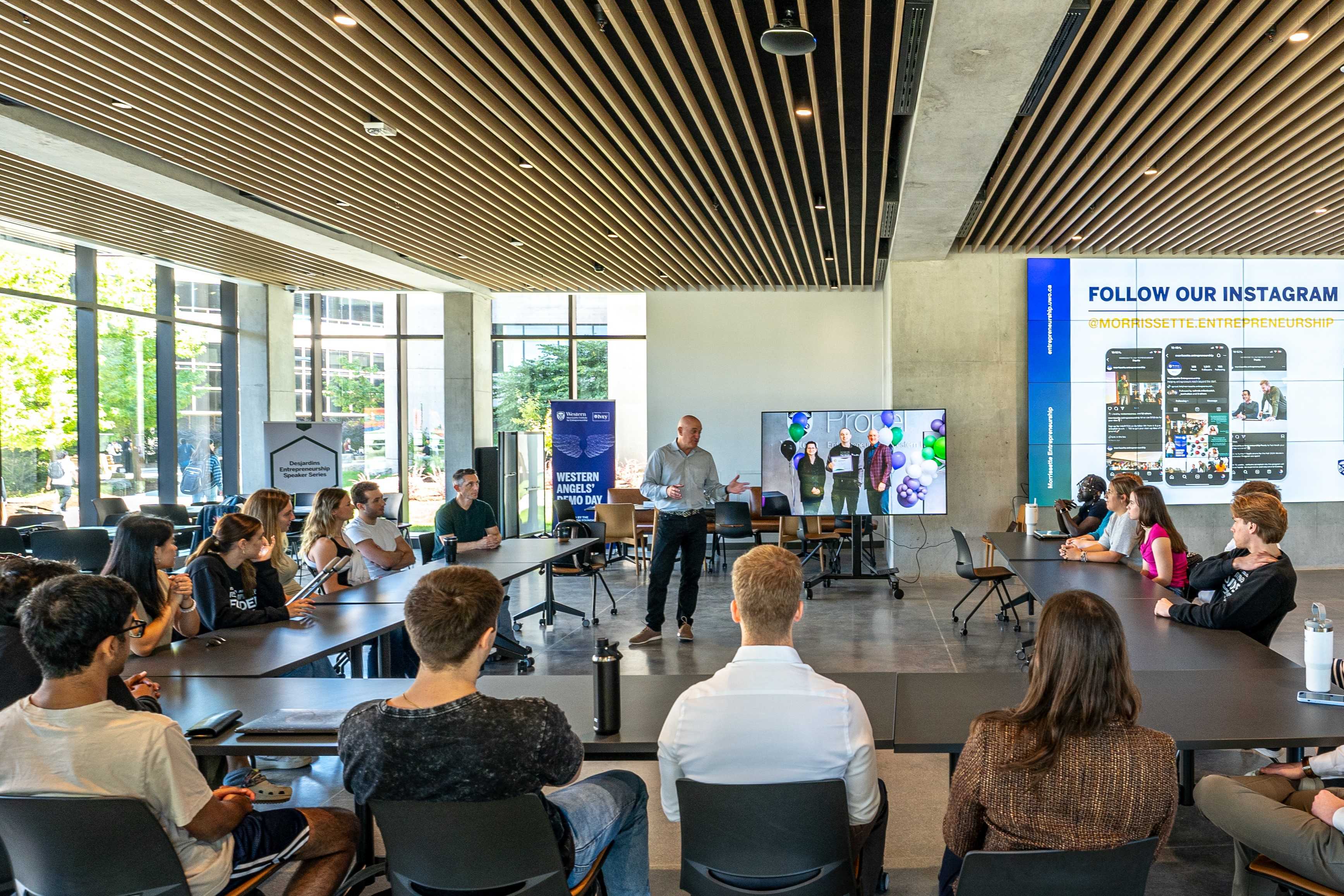 A workshop speaker leading a discussion with students around a table.